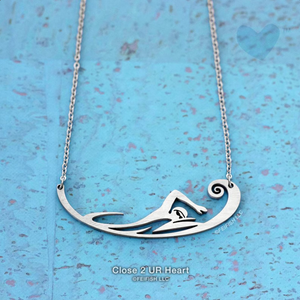 A stainless steel necklace pendant featuring an abstract swimmer with small waves, accented with a wave curl, by Close 2 UR Heart.
