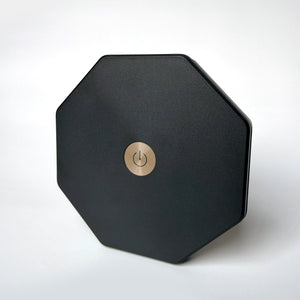 A matte black octagonal electronic device with a circular gold power button in the center, shown on a clean white background.