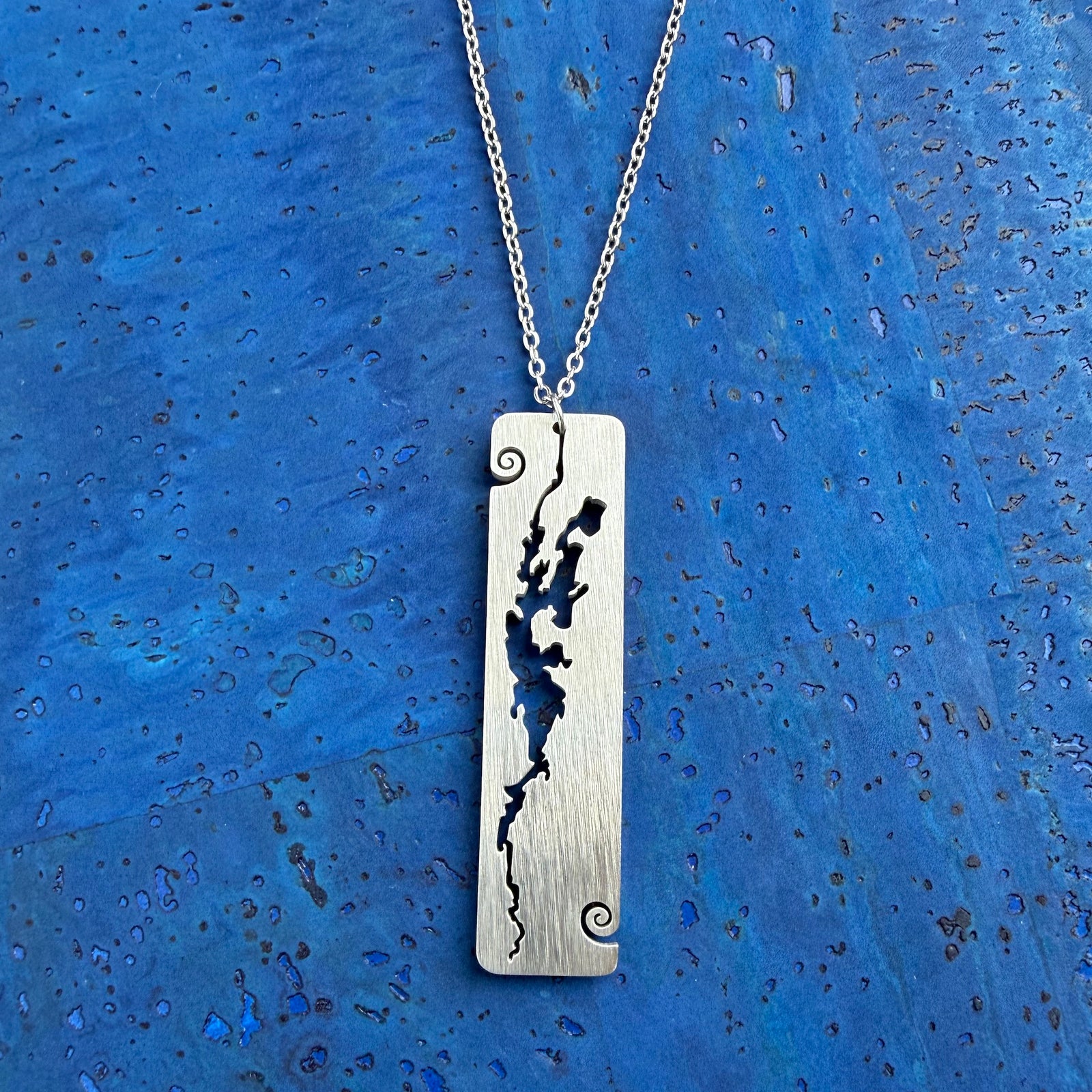 A stainless steel rectangular-shaped necklace pendant featuring a cut-out shape of Lake Champlain, with wave curl accents, by Close 2 UR Heart.