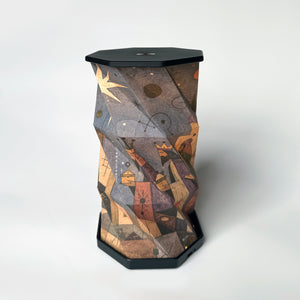A sculptural, hexagonal side table or lamp featuring a faceted, twisted design covered in an abstract, geometric art print. The print depicts figures and star-like motifs in warm earth tones of brown, beige, and orange, set against a dark charcoal/black base and top surface, photographed on a clean white studio background.